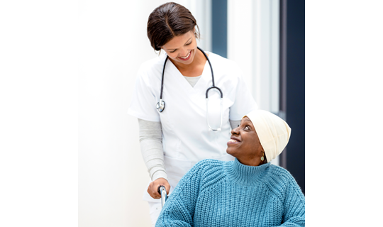 nurse in white scrubs pushing oncology patient wearing blue sweater in wheel chair