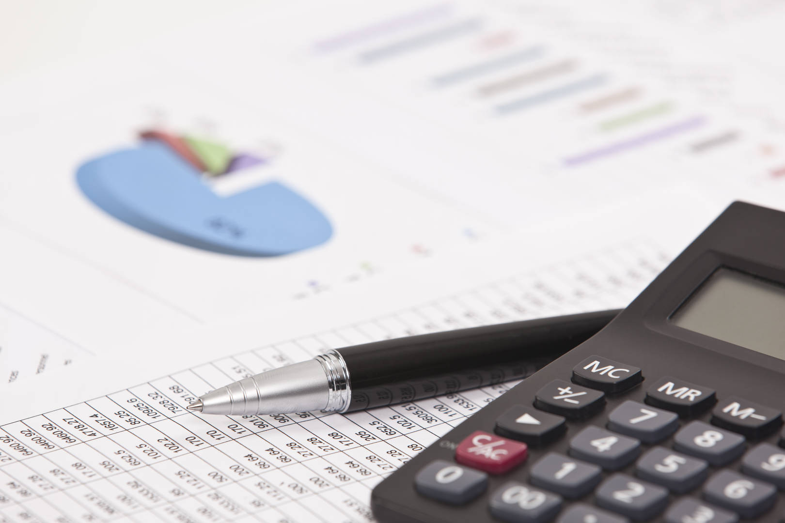 Calculator beside a pen and financial analysis paper